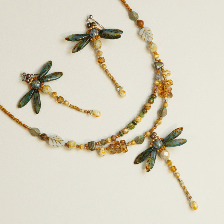 Detail van libelle met blauwgroene vleugels als middelpunt van een kralenketting in warme aardetinten