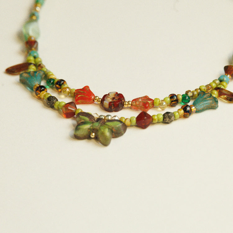 Detail van de vlinderhanger en groene kralen in een handgeregen ketting van Tsjechisch glaskralen.