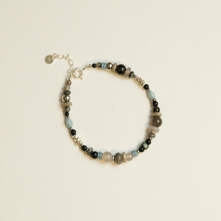 Handgemaakte kralenarmband met zwarte agaat, labradoriet en zilveren details, plat liggend weergegeven.