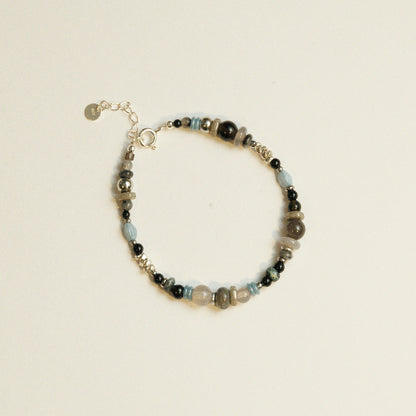 Handgemaakte kralenarmband met zwarte agaat, labradoriet en zilveren details, plat liggend weergegeven.